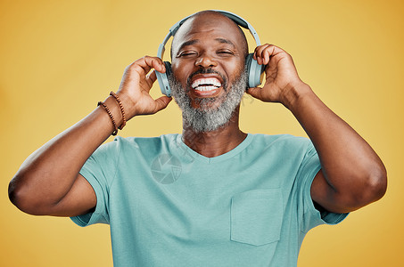 快乐成熟的非洲裔美国人独自站在工作室的黄色背景下 戴着耳机听音乐 留着灰胡子享受音乐的高级黑人微笑肖像乐趣冒充男人技术胡须自由姿背景图片