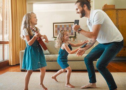 年轻快乐的父亲和他的小女儿们在家里的休息室里唱歌跳舞 快乐的小兄弟姐妹弹吉他 在家里和爸爸一起玩背景图片