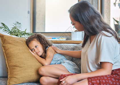 悲伤沮丧的小女孩躺在沙发上 看着别处 而担心的母亲心理学家试图与她交谈 慈爱的母亲试图与心烦意乱的女儿沟通 年轻的西班牙裔母亲在背景