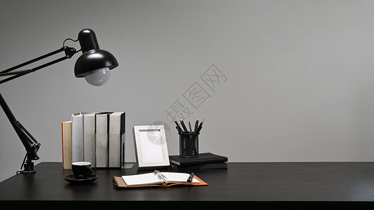空白的画框 书本 铅笔架和黑桌上的灯具背景图片