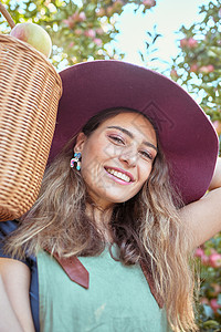 刚摘下苹果在阳光明媚的日子里 一位快乐的女人拿着一篮子从可持续果园农场树上摘下的新鲜苹果的画像 欢快的农民的脸在时令收获多汁的有机水果吃背景