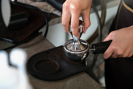 一名女工在咖啡机安装之前 用篡改棒按烤咖啡豆的搅拌器来施压背景图片