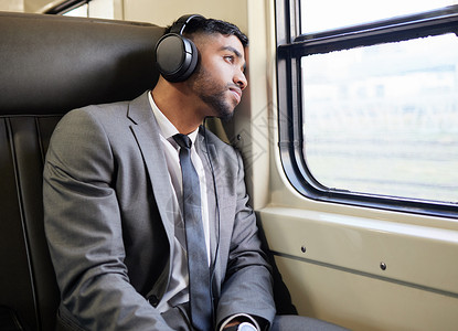 坐下来想了一会儿 一个年轻的商务人士在上下班途中戴着耳机凝视着窗外背景图片