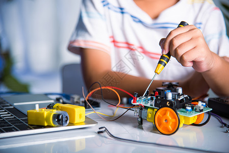 亚裔男孩在家里组装Arduino机器人汽车家庭作业项目学习活动教育俱乐部课堂作坊男生孩子科学发明背景