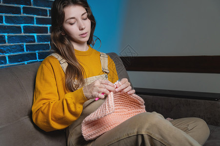 女孩坐在沙发上 用纱布编织毛衣 我们用厚的线织在一起 安居乐业钩针针织品纺织品手工女士工作工艺编织者针线活棉布背景图片
