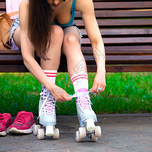 女性滑冰者在公园的长凳上绑着溜冰鞋鞋带刀片长椅齿轮滑冰乐趣运动装溜冰者冰鞋女孩背景图片