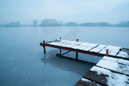 被雪覆盖码头在冰冻湖的码头上下雪背景