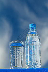 塑料板上水瓶和水杯 底底有蓝天的蓝色天空背景图片