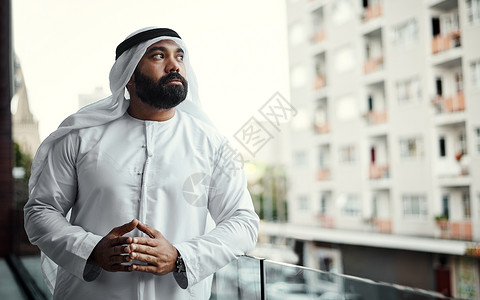 他在阳台上竭尽全力思考 一位身着传统伊斯兰服装的商务人士在他办公室的阳台上工作背景