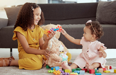 可爱的混血儿在家里的客厅里和小妹妹玩耍 两个可爱的西班牙裔小女孩坐在一起玩玩具和毛绒玩具时亲密无间 微笑的兄弟姐妹背景图片
