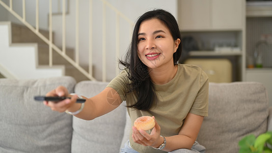 带遥控器的年轻亚洲女性在家看搞笑电视喜剧电影背景图片