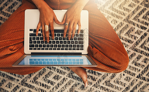 在家庭客厅使用笔记本电脑写博客的不知名混血女性的上方视图 西班牙裔企业家独自盘腿坐在休息室的地板上 输入有关技术的博客文章 远程背景图片
