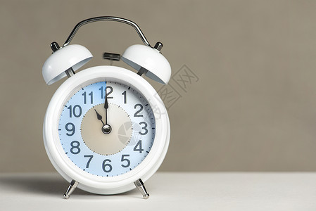 时钟10点十一点闹钟 一个白色的闹钟在一张白色的桌子上 时钟指针指向 11 点 时间更改为夏令时或冬令时 设置 11 00 或 23 00背景