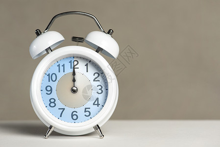奋斗12点十二点闹钟 一个白色的闹钟在一张白色的桌子上 时钟指针指向 12 点 时间更改为夏令时或冬令时 将闹钟设置为 12 00 或 2背景