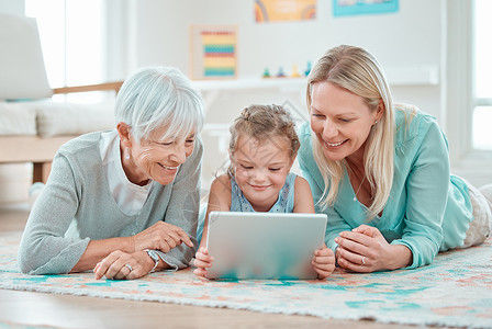 我们希望在成长过程中拥有这些工具 一个可爱的小女孩和她的母亲和祖母躺在家里使用数字平板电脑背景图片