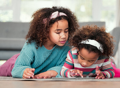 同舟共济共度难关两个小女孩在家里一起玩数字平板电脑游戏 和两个女孩共度难关背景
