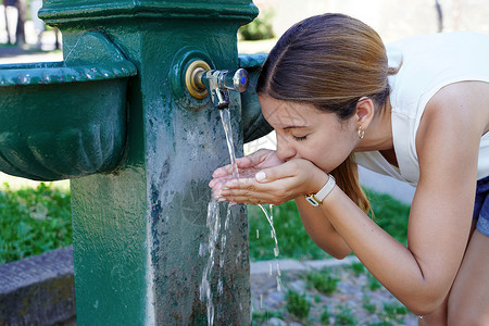 缺水的女孩紧急缺水 年轻女性在城市热量暴涨时从喷泉里取水水背景