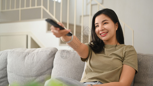 身着散衣的年轻亚洲妇女睡在沙发上 在舒适的家中看有趣的电视喜剧电影背景图片