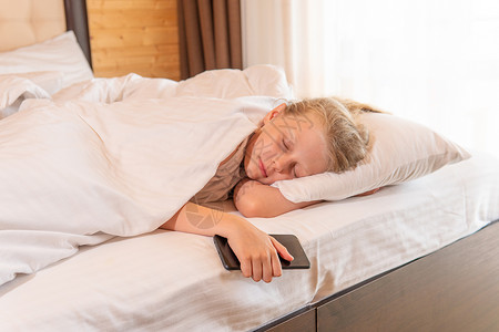 睡觉手机女孩美丽的年轻床毯睡在早上 概念白色亲自放松 微笑积极 健康美丽 室内宁静的乐趣背景图片