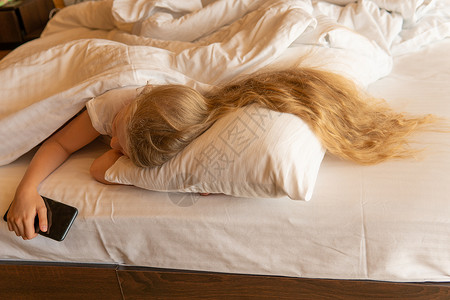 睡前女孩移动美丽的年轻手机床毯房 供来自宁静床上 健康放松的人的女枕头使用 在门内休息日背景图片