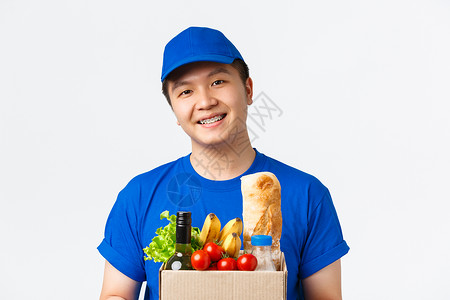 网上购物 食品送货和货运概念 特写微笑般愉快的像男性信使 穿着蓝制服 把装有杂货单的箱子交给客户 站立白背景背景图片