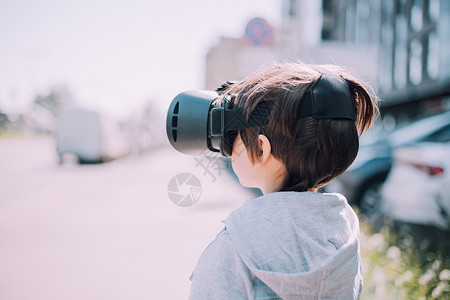 一个男孩在街上玩虚拟现实眼镜 现代小玩意 儿童游戏 虚拟眼镜的选择 一篇关于虚拟眼镜的文章 现代儿童树木旅行乐趣金发女郎公园技术背景图片