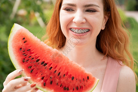 西瓜来了美丽的红发美女 带着牙套微笑着 夏天就要在户外吃一片西瓜了牙医金属季节治疗学生化妆品蔬菜活力青年水果背景