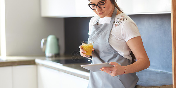 厨房有橙汁和石板的年轻女子家庭技术互联网女性玻璃商务橙子药片早餐头发背景图片