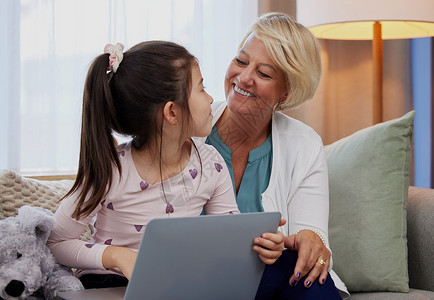 我看到你一直在关注我最喜欢的节目 一个可爱的小女孩和她的祖母坐在家里使用笔记本电脑背景图片