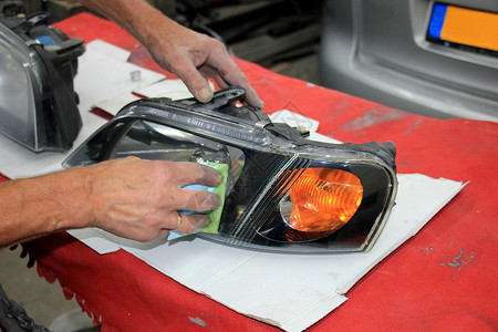 男子用清晰的涂层整修车头灯机器车辆维修抹布机械损害修复身体汽车店铺背景图片