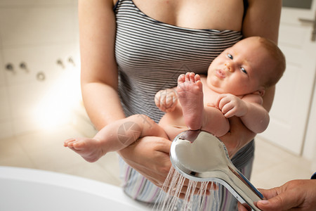 婴儿淋浴母亲在淋浴时洗完凳子后为婴儿洗澡新生家庭男生手臂身体孩子卫生女士浴室女性背景