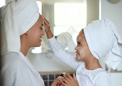 母亲和女儿在家里的水疗日里亲密无间 共度时光 小女孩在微笑和玩乐时涂抹面霜 做皮肤面部护理的快乐妈妈和孩子背景