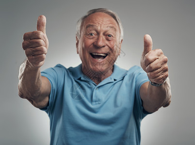 一个快乐的老人 在一个工作室里用灰色的背景来举起拇指 我们当然应该再做一次背景图片