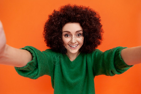 快乐的非洲发型女子穿着绿色随身毛衣 自己做POV 表达积极情绪 装腔作势 笑得像牙一样背景图片