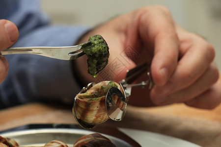 蜗牛食物男人用特别的叉子和蜗牛叉来吃布哥根咖啡饼香菜黄油烹饪蜗牛绿色美食食物草本植物田螺昆虫背景