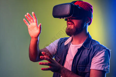 虚拟现实器令人印象深刻的长胡子时髦男子站在VR 玩电子游戏和试图触摸的东西背景