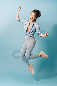 一个快乐的年轻女子跳跃和庆祝浅蓝背景的全长肖像 片名工作室闲暇女孩乐趣女性牛仔布背景图片