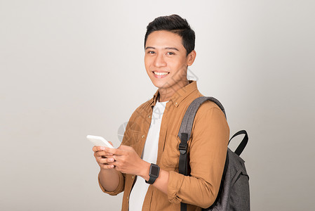 亚洲青年学生在白种背景上孤立的手机上发短信电话写作青少年背包发型男生男人牛仔裤微笑阅读背景图片