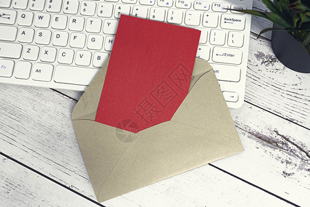 敬请棕色信封里有红色便条 键盘和木质桌上的陶工厂广告邮政投资记事本推介会回复床单特权卡片服务背景