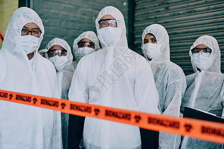 毒面具身着保护性排泄物以防止病毒在检疫地点传播的Covid 大流行病和团队医生 科学家或保健工作者 头等应答人员站在磁带后面时穿着哈兹背景