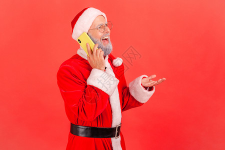 穿着圣诞老人服装 留着灰色胡须 面带微笑的老人在电话里说话 面带积极的表情 令人愉快的消息背景图片