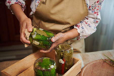 细节 女性家庭主妇手握着一罐泡黄瓜的玻璃罐头 倒放在木箱上背景