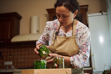 时令已快到惊蛰有魅力的家庭主妇煮自制泡菜 用瓜子罐头 倒在厨房的木纸箱上背景