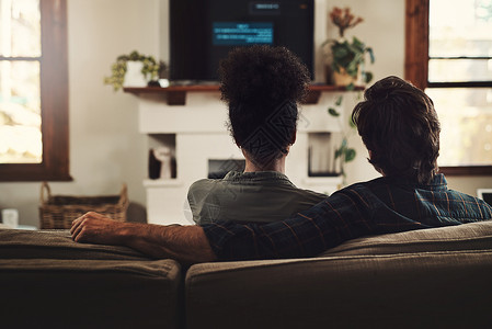 在沙发上坐着一对年轻夫妇的回视镜头 在家里一起看电视 然后我们再看看他们的照片吧?背景图片