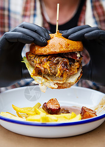 快餐和外卖食品的概念 一个戴着黑色乳胶手套的男人手里拿着一个多汁的汉堡包 靠近金属盘上的炸薯条和奶酪酱 特写背景图片