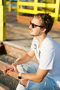 身戴太阳镜的年轻人坐在木制阶梯上背景图片