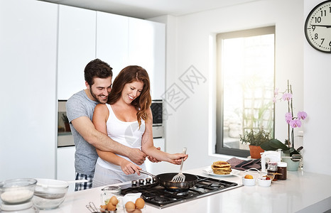 我们可以多吃点这样的早晨 早上准备早餐的一对快乐的年轻夫妇一起来做这个背景图片