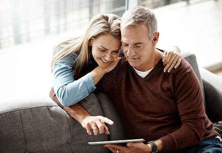 只需轻按一下 即可享受情侣假期 一对成熟的夫妇在家里的沙发上一起放松时使用数字平板电脑背景图片