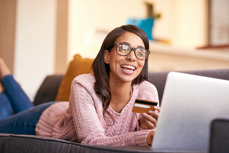 当您放松时 购物疗法会更好 一个迷人的年轻女人在家里的沙发上使用笔记本电脑和信用卡背景图片