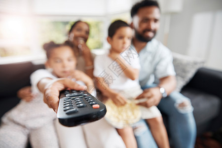 电视连续剧解读与家人一起在客厅看电视的遥控器特写 父母和孩子在沙发上放松 在家里的休息室里看电影 连续剧或卡通片 同时保持亲密背景